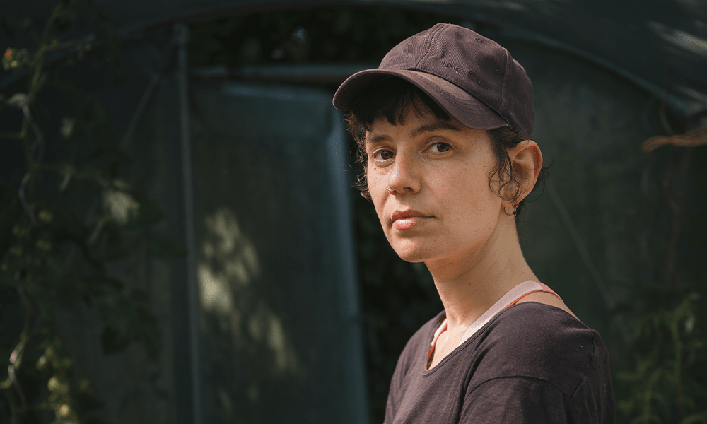 Juliette Rousseau regarde l'objectif sur un fond de jardin. Elle porte une casquette.